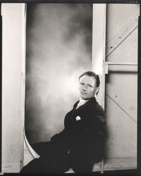 George Platt Lynes, Christopher Isherwood, ​n.d. Subject is seated leaning to the right against a wooden studio wall.