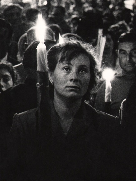 Mario Finocchiaro, Sant'Alfio, Sicilia, ​1958. A woman holds a large lit candle in a crowd of people doing the same.