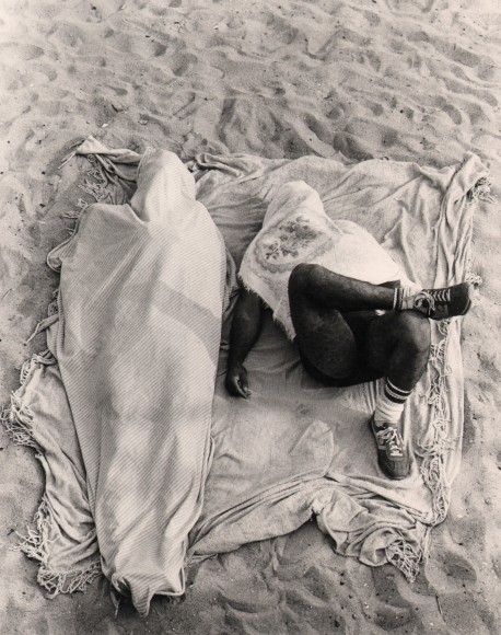 11. Beuford Smith, Coney Island, ​1979. Two figures photographed from above lay on a blanket on the sand, both have blankets covering their bodies as well.