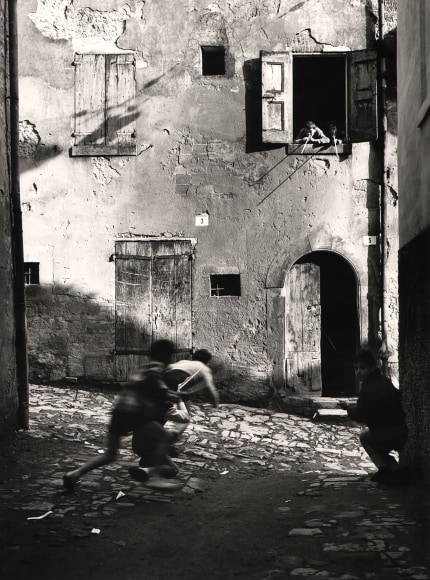 Nino Migliori, The Street Kids, 1955. Five boys play with peashooters in an alley. Three are on the street, two are leaning out a second story window.