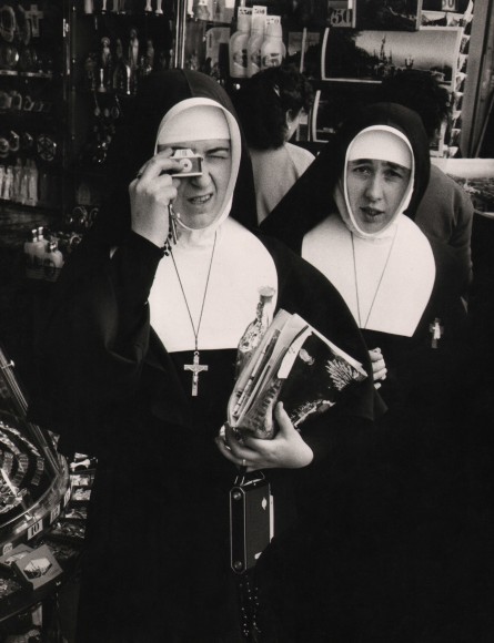 38. David Moore, Nuns at Lourdes, c. 1959. Two nuns look to the photographer, one holding a miniature camera to her face.