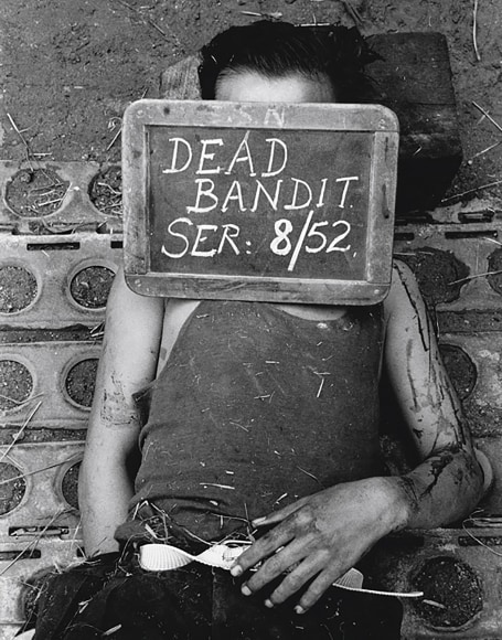 28. Howard Sochurek, Communist in Malaya, ​1952. A small body with blood on arms and a sign over the face that reads &quot;Dead bandit ser: 8/52&quot;
