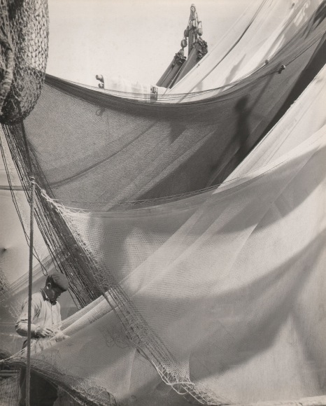 Ezio Quiresi, Reti Chioggiotte, ​c. 1952. A man stands in the lower left of the frame, netting draped all around him. He looks down at one section of netting.