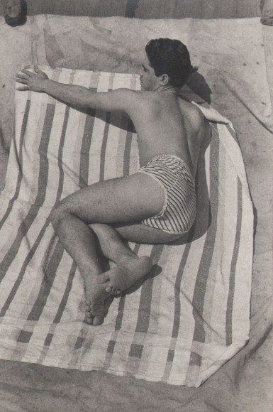PaJaMa, Jos&eacute; Martinez, ​c. 1945. A man in a swimsuit lays on a striped towel, facing left.