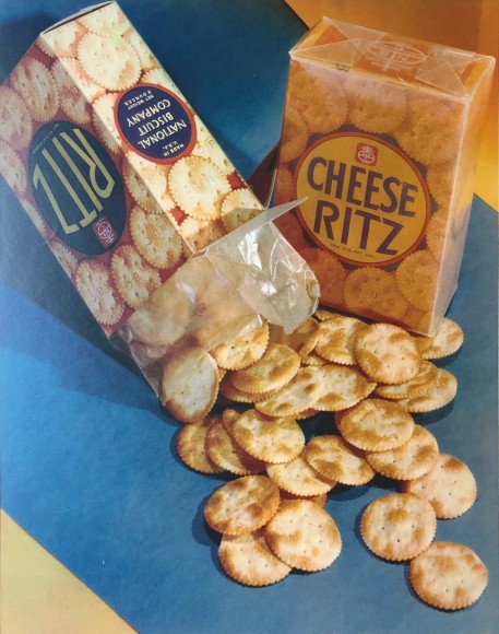 Harold Haliday Costain, Ritz Crackers, ​c. 1937. &quot;Ritz&quot; and &quot;Cheese Ritz&quot; boxes on a blue and yellow surface. The &quot;Ritz&quot; box is tipped so that crackers have spilled out.