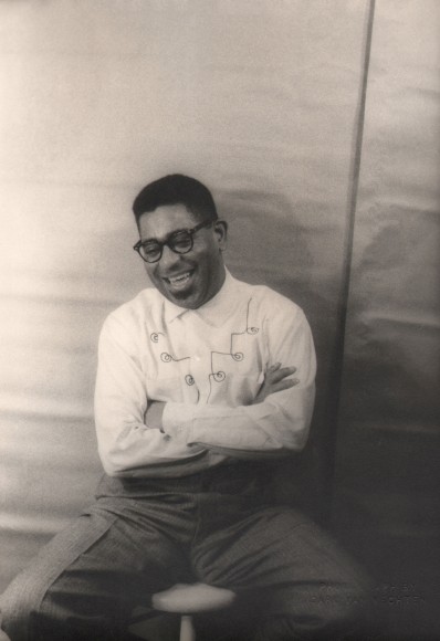 Carl Van Vechten, Dizzy Gillespie, ​1955. Subject is seated with arms crossed, smiling with eyes cast down to the left.