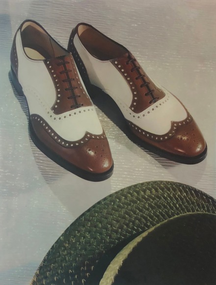 Harold Haliday Costain, Whitehouse and Hardy Shoes, ​1937. Brown and white brogue shoes beside a green hat in partial view.