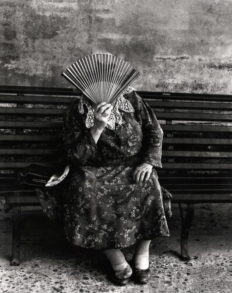 Nino Migliori, People of the South, 1956. A woman seated on a bench, holding a paper fan in front of her face.