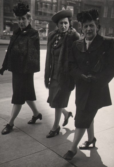 27. Jeanne Ebstel, Untitled, c. 1945. Three women in dark coats, hats, and gloves walk on the sidewalk.