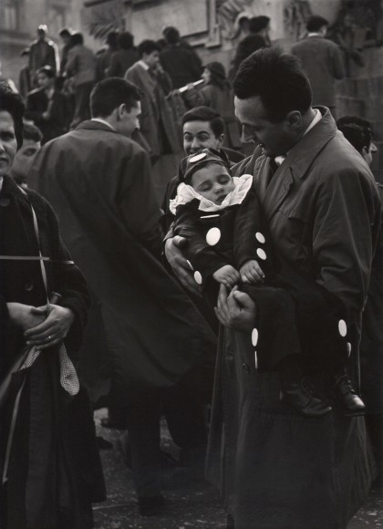 Ugo Zovetti, Untitled, ​1960. A man stands in a crowd cradling a young boy in a spotted costume who appears to be sleeping.