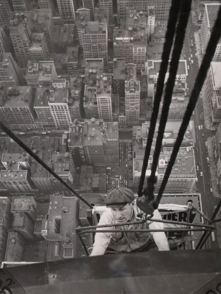 15. Associated Press, Nice Work if You Can Take It, ​c. 1931. Downward-looking view of a man supported by thick ropes suspended against a building. The city can be seen far below and behind him.