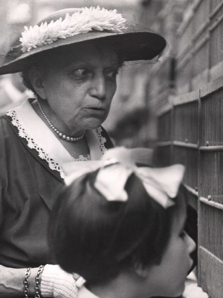 Ugo Zovetti, Allo Zoo, ​c. 1960. An older woman in a hat and pearls looks warily into a cage alongside a young girl with a white bow in her hair.