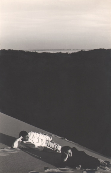 PaJaMa, Paul Cadmus, Margaret French, Provincetown, ​c. 1947. Two figures recline on a sand dune in the foreground. Midground is all in shadow, and in the background sea and sky.