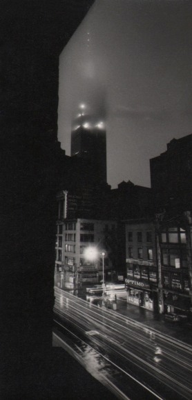30. W. Eugene Smith, As From My Window I Sometimes Glance, ​1957&ndash;1958. Nighttime view of a city street. The Empire State building is in the center background shrouded in fog.