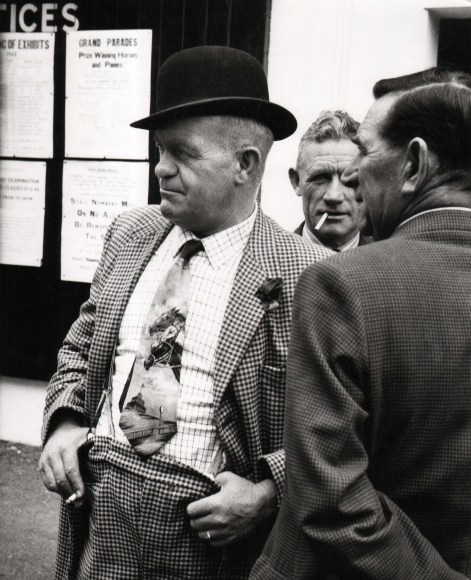 26. Brian Seed, Untitled, ​c. 1954&ndash;1966. A man in a bowler hat and checkered suit looks to the left of the frame with two other men.
