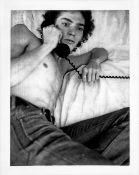 Self-Portrait of the artist on bed, holding phone.