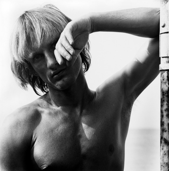 Man leaning propping his arm up against a rusty wall with one hand hanging in front of half his face.