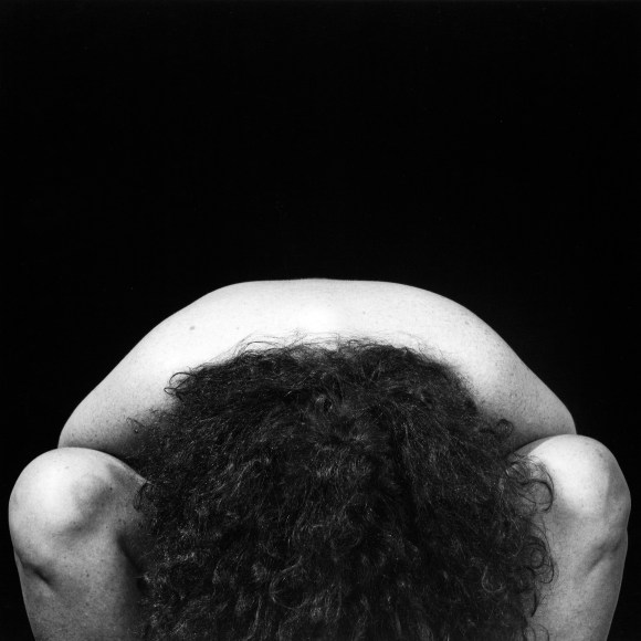 Woman with dark wavy hair sitting and hanging her head down between her legs.