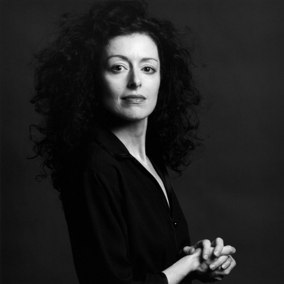 Close-up of a woman turning to look at the viewer and clasping her hands in front of her chest.