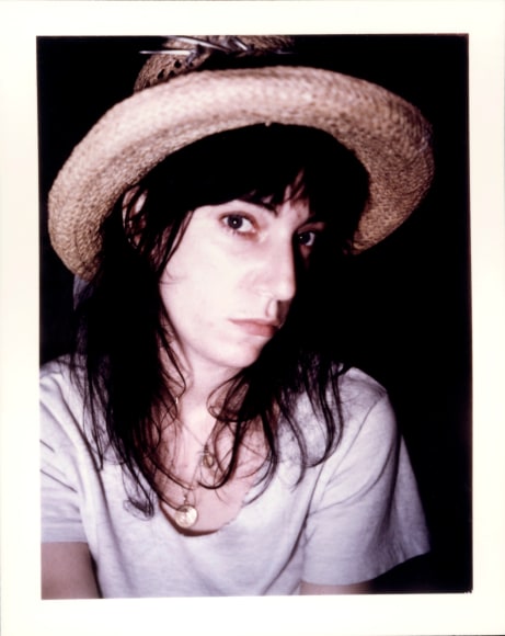 Close up of a woman in a white t-shirt and straw hat with black hair looking into the camera.