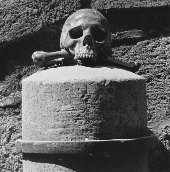 Skull and crossbones on a large stone plinth in front of a rough stone wall.