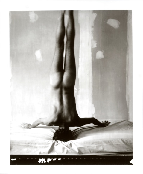 Naked man facing away from the camera doing a headstand on a bed.