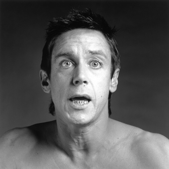 Shirtless Iggy Pop from the chest up, mouth open and eyes wide.