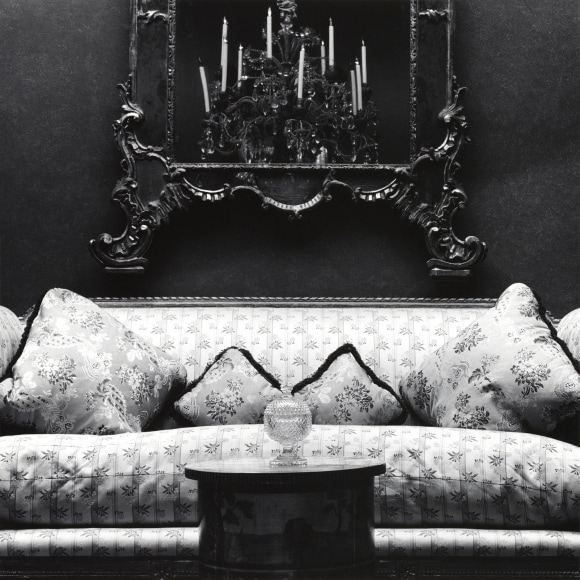 Patterned couch, centered, with mirror on wall behind and table with glass object in front.