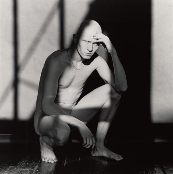 A man crouching in an interior, a geometric shadow is cast over his body.