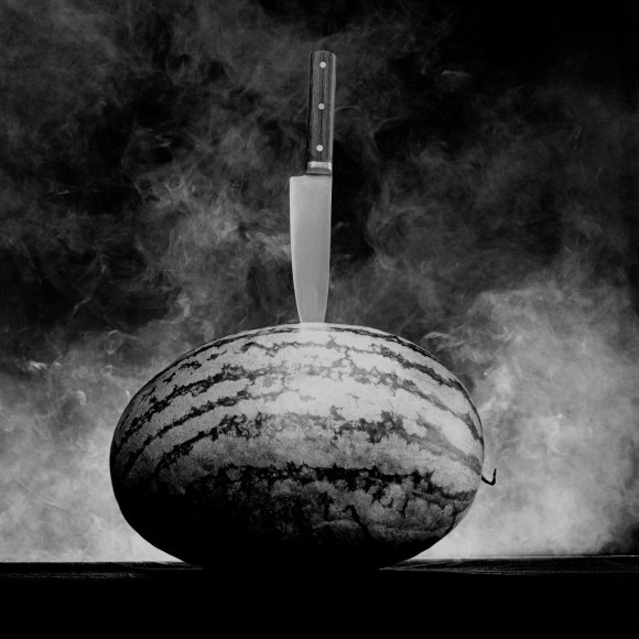 Full watermelon with knife stuck in center.