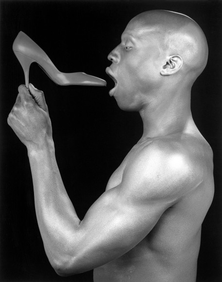 Ken Moody in profile, holding a high heeled shoe close to his mouth.