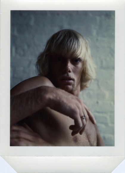 Shirtless man from the chest up turning to look at the viewer.