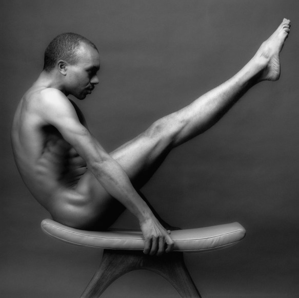 Nude black man on balance beam with legs up