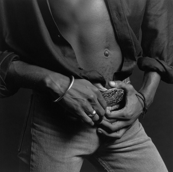 Black male wearing unbuttoned shirt and jeans, hands holding belt.