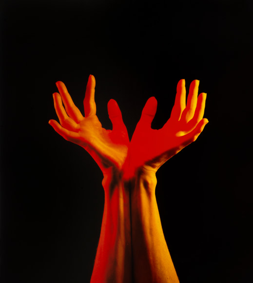 Woman's hands and wrists reaching up against a black background.
