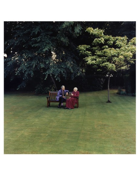 Portrait of two men sitting on a bench in a green field.