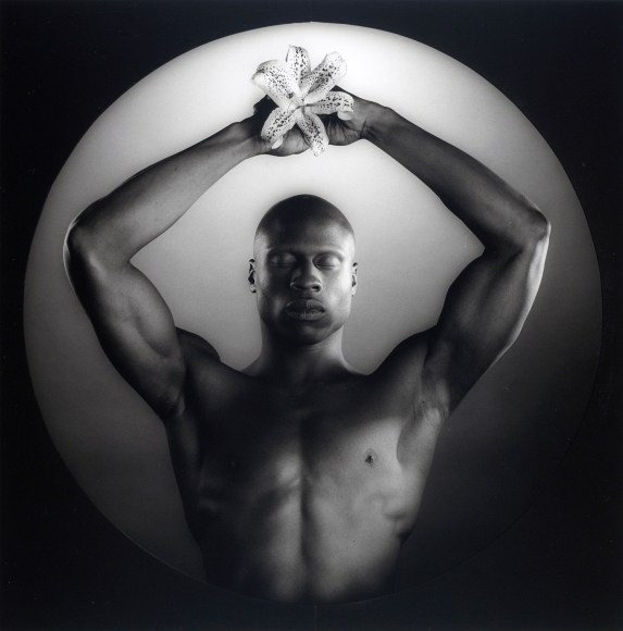 Ken Moody holding a flower up above his head, with eyes closed.