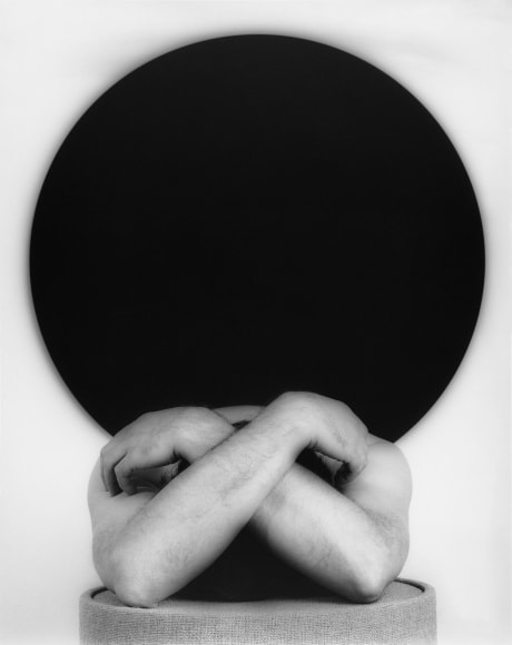 Man covering his head with both arms. Black circle behind him.