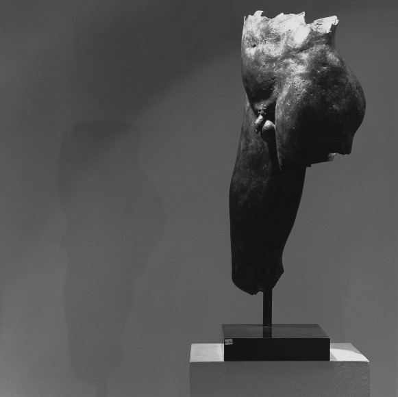 Bronze sculpture of male torso to knee-cap on a pedestal.