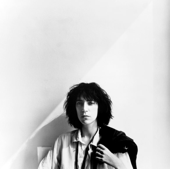 Portrait of Patti Smith holding a black jacket over her shoulder.