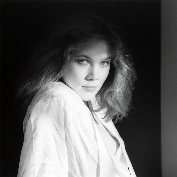 Kathleen Turner wearing a white shirt staring at the camera.
