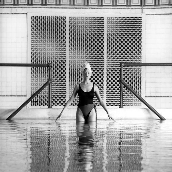 Woman partially submerged in pool, hair up in towel.