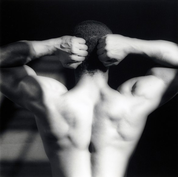 Vibert, with hands on head, facing away from camera shirtless.