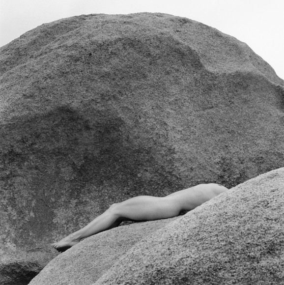 Lisa Lyon lying on rocks nude back is ached and head is hidden.