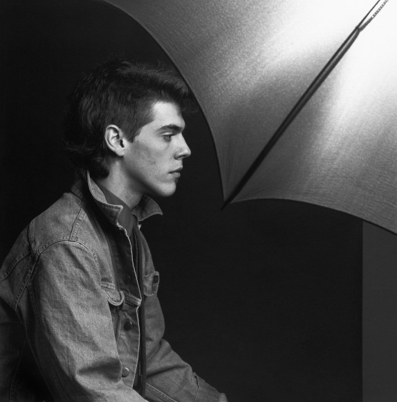 Profile view of young man wearing a denim jacket sitting in front of the visible reflecting umbrella from the studio set-up.