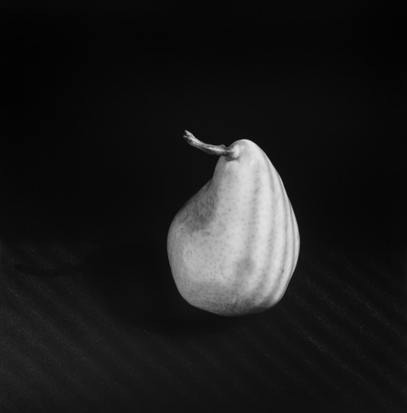 Pear atop shadowed table with dark background.