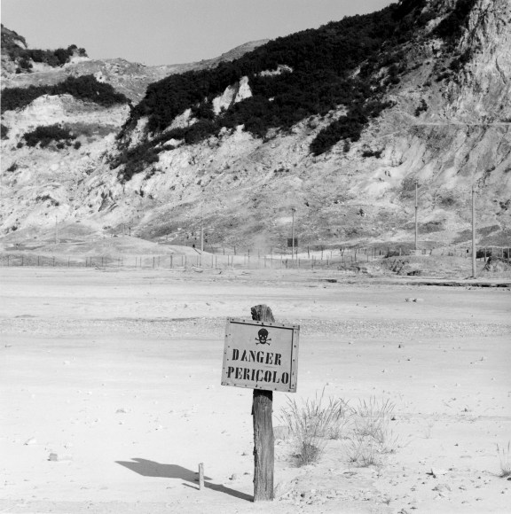 Sign with &quot;Dancer Pericolo&quot; and a skull in the foreground, mountains in background.