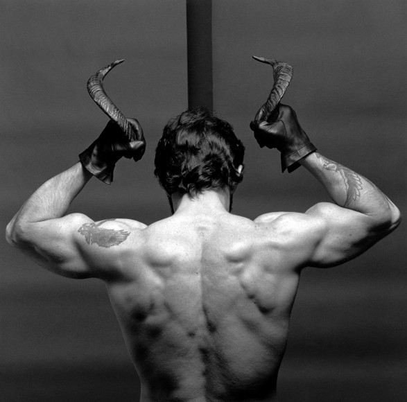 Nude white man facing away from camera from the torso up, holding horns.