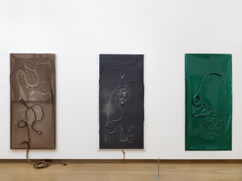 Three vacuum rope works that are vertically long. From left to right, the works are monochrome: brown, black, and dark green.