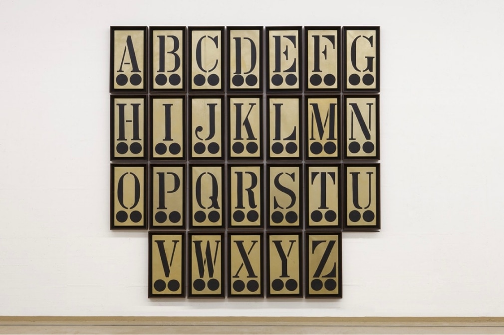 The Black Alphabet is a painting consisting of twenty-six 24 by 12 inch gold panels, each with a different letter of the alphabet in black above to black circles. In the image the painting is displayed in four horizontal rows: the firs with the letters A through G, the second with the letters H through N, the third with the letters O through U, and the last with the letters V through Z.
